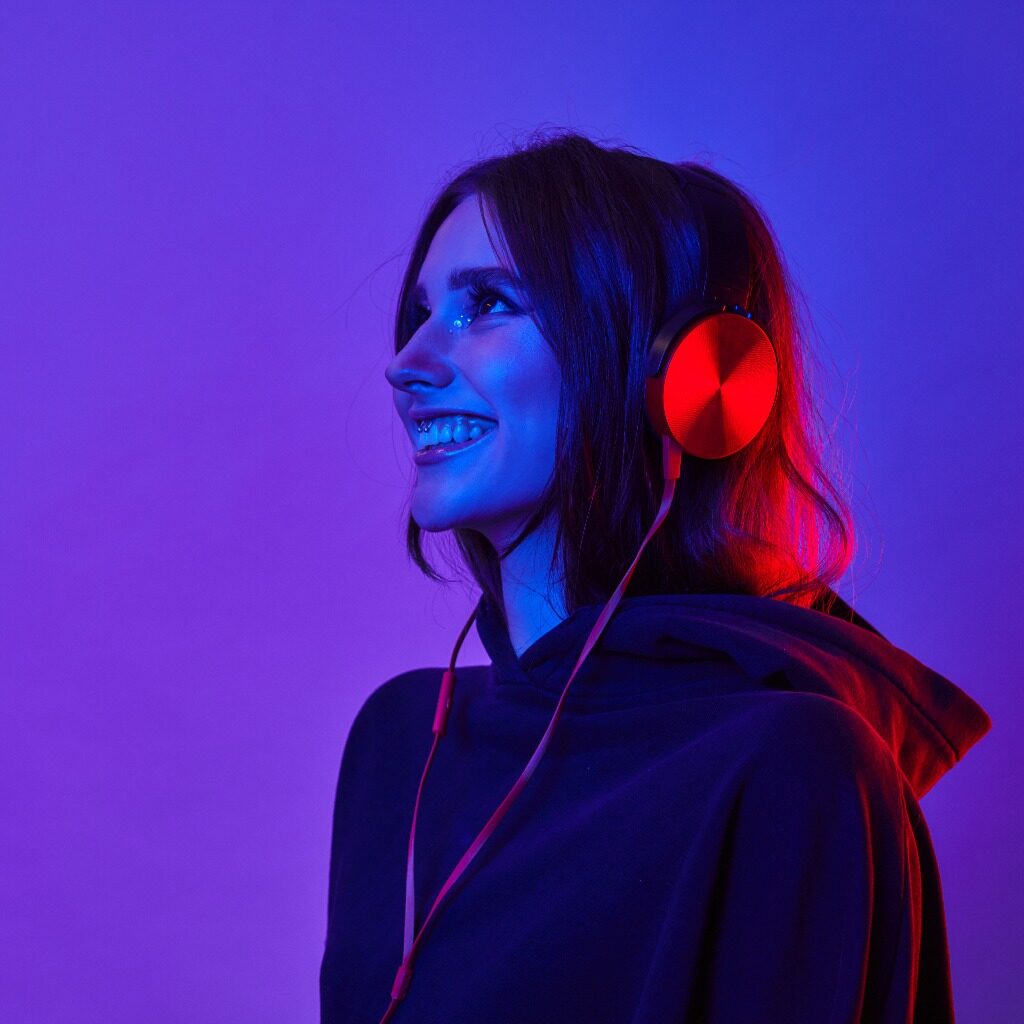 Fashion hipster woman smiles and wear headphones listening to music over color neon background at studio jpg